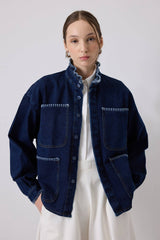 Person wearing a dark blue denim jacket over a white shirt and pants on a light gray background